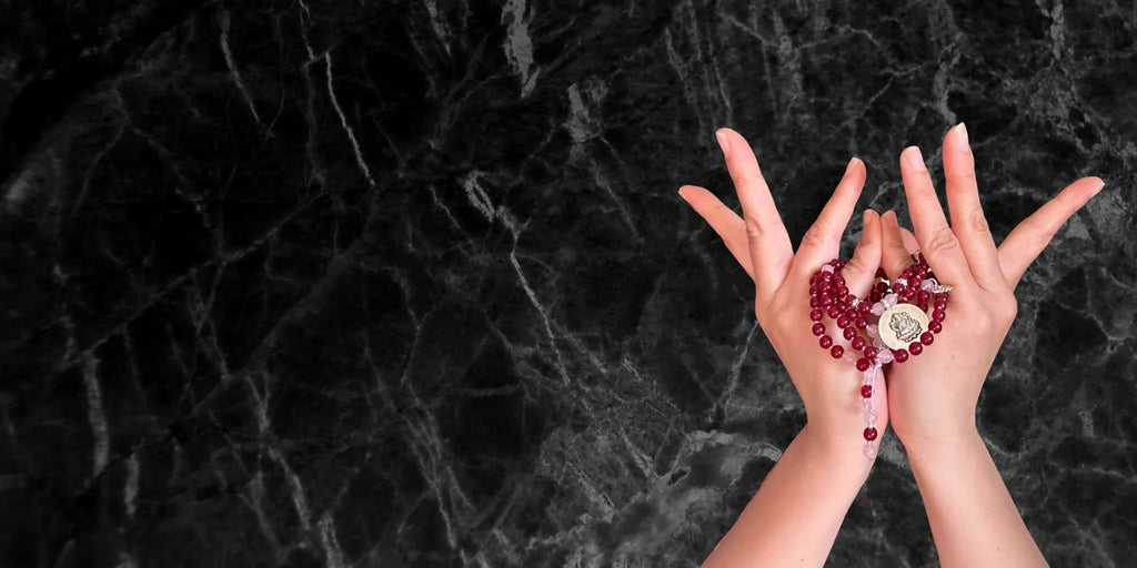 Mani in mudra con japamala, simbolo dei materiali e dei componenti sacri che la compongono. Hero desktop della pagina Umadevi dedicata alla struttura e agli elementi di una japamala.