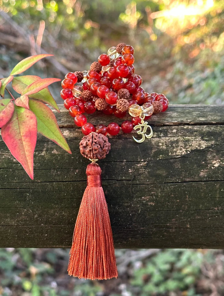 Japamālā Diwali in Rudrākṣa, Corniola e Quarzo Citrino adagiata uno steccato di legno, con luce dorata e foglie.