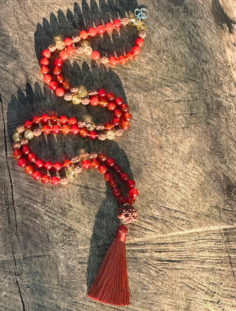 Japamālā Diwali in Rudrākṣa, Corniola e Quarzo Citrino disposta per lungo su un tronco, per mostrare il modello completo con pendente Oṃ e nappina.