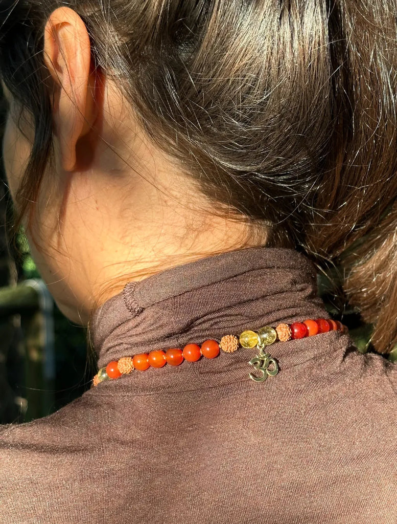 Dettaglio del pendente Oṃ in argento dorato della Japamālā Diwali, visibile dietro al collo quando indossata lunga.