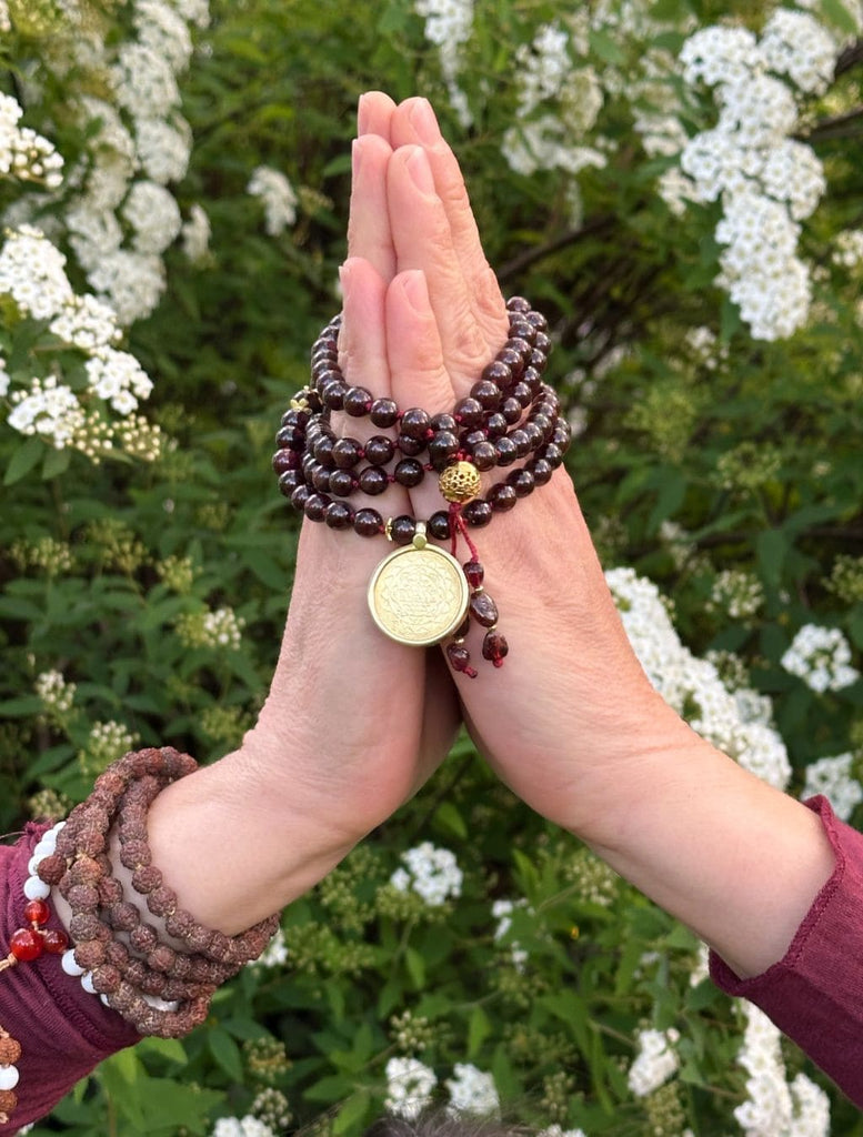 Japamala spirituale con simbolo Śrīyantra e pietra Granato - tra le mani in namaste
