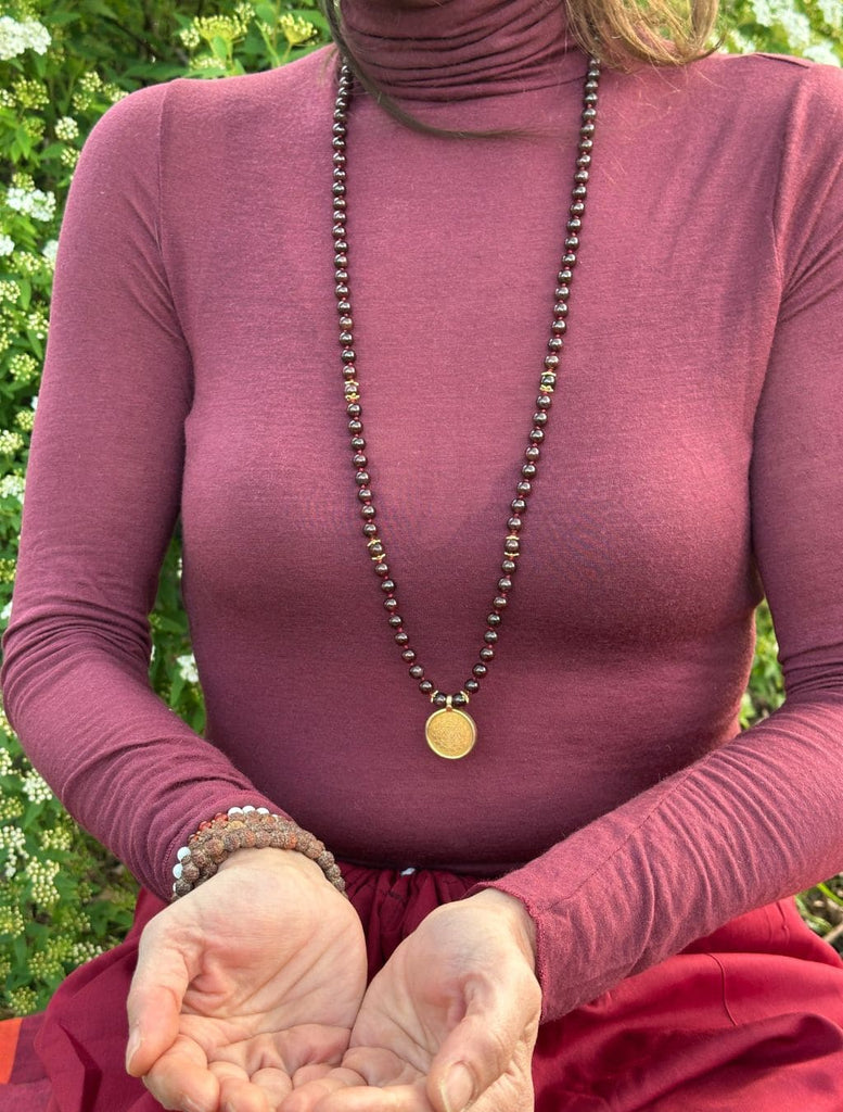 Una japamālā da 108 +1 grani, realizzata a mano con Granato naturale e il sacro simbolo dello Śrīyantra indossata