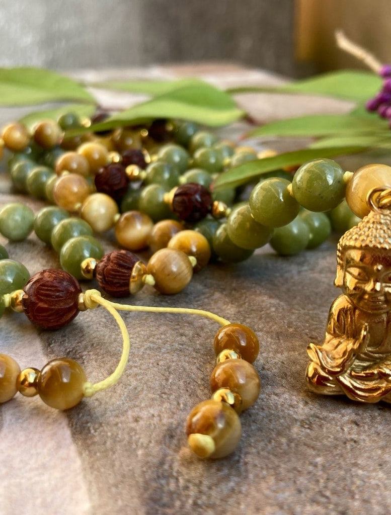 Japamala in giada verde, occhio di tigre, legno di sandalo. Zoom sui dettagli del  pendente Buddha e sugli intarsi a forma di fiore di loto presenti sul legno di sandalo

