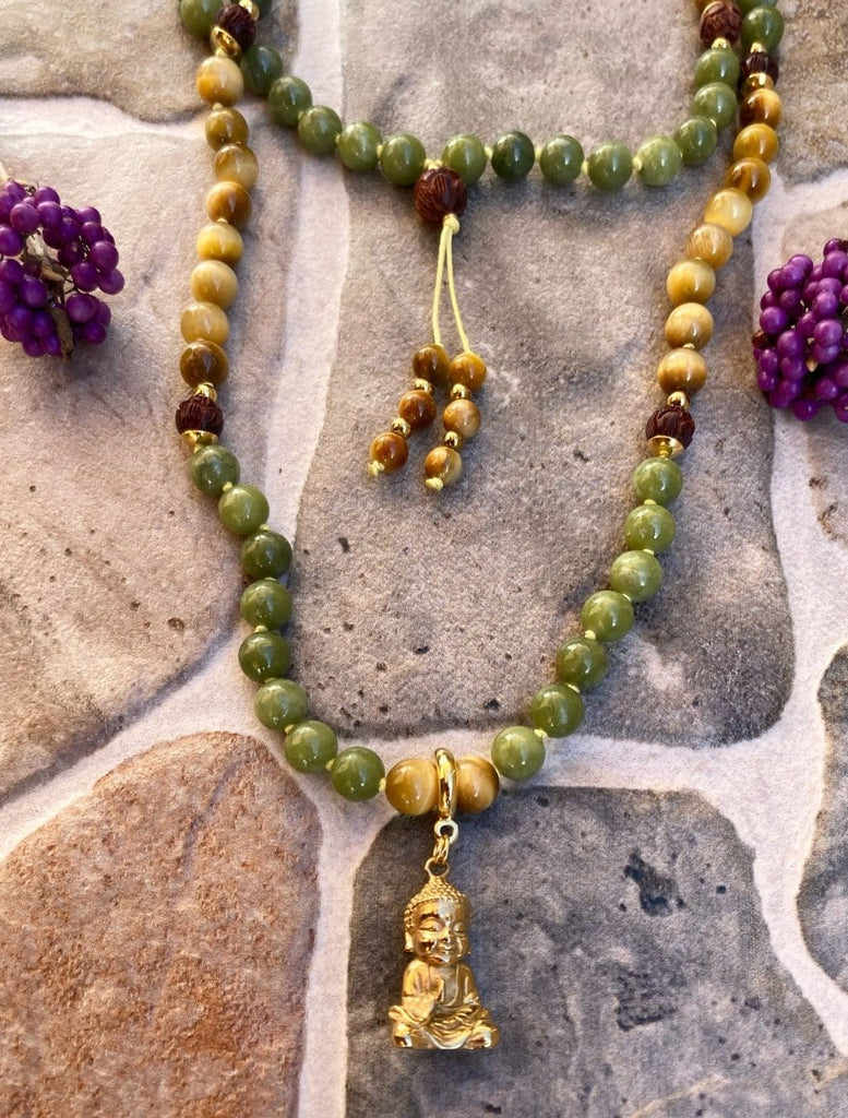 Japamala in giada verde, occhio di tigre, legno di sandalo e pendente ottone Buddha. Adagiata su una superficie per mostrare come si indossa con doppio giro intorno al collo. 