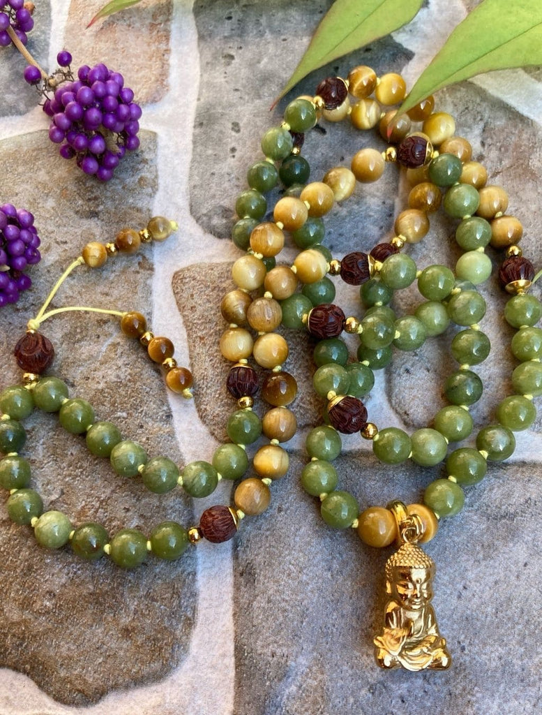 Japamala in giada verde, occhio di tigre e legno di sandalo intarsiato a forma di fiore di loto. Zoom sui dettagli della lavorazione artigianale e sul pendente ottone Buddha. 