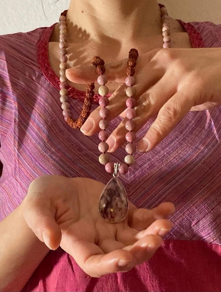 japamala fatto a mano con pietre di rodonite e semi sacri di rudraksha. Tenuto tra le mani per mostrare dettagli e caratteristiche