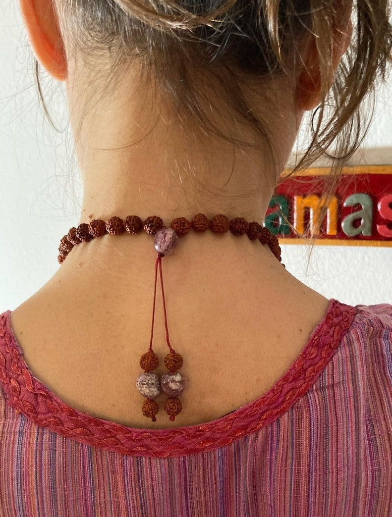 japamala fatto a mano con pietre di rodonite e semi sacri di rudraksha. Zoom sul grano e i terminali posti dietro al collo della modella che li indossa