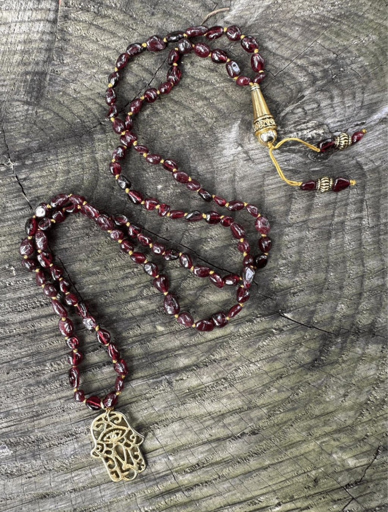 Japamala 108 sassolini di Granato e pendente ottone mano di Fatima disposto in lunghezza per mostrare design.