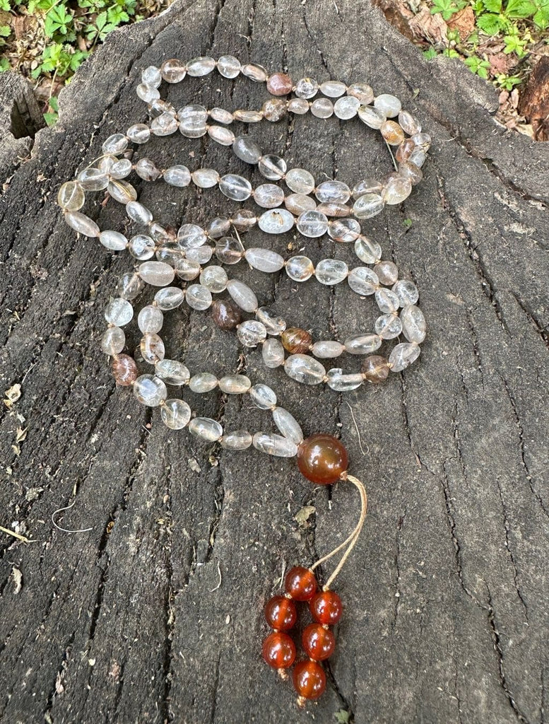 Japamala composta da 108 sassolini in quarzo rutilato e corniola, distesa per lungo per mostrare il design dettagliato e l'eleganza naturale, ideale per meditazione e consapevolezza spirituale.