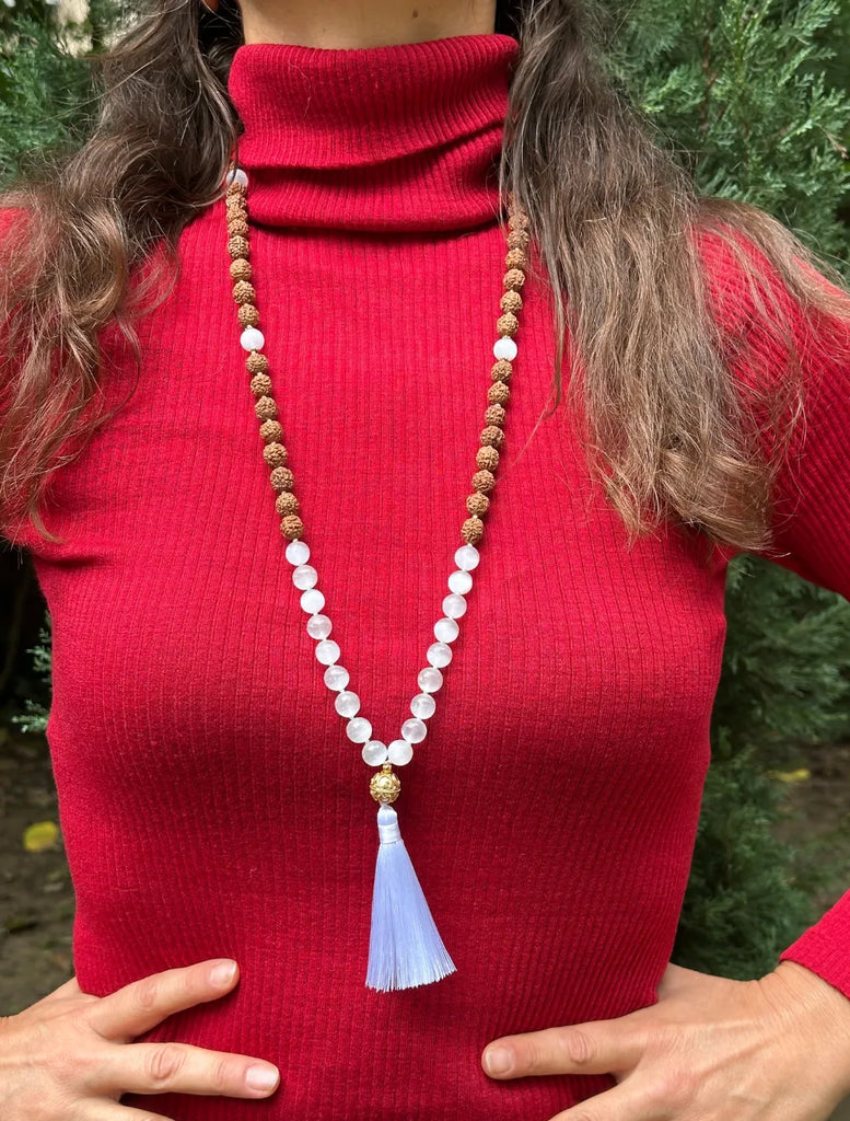 japamala in selenite e rudraksha indossata, con pendente OM e nappina bianca in evidenza.