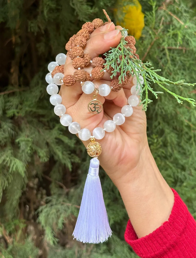 japamala in selenite e rudraksha tenuta tra le mani con pendente OM in argento dorato e nappina bianca