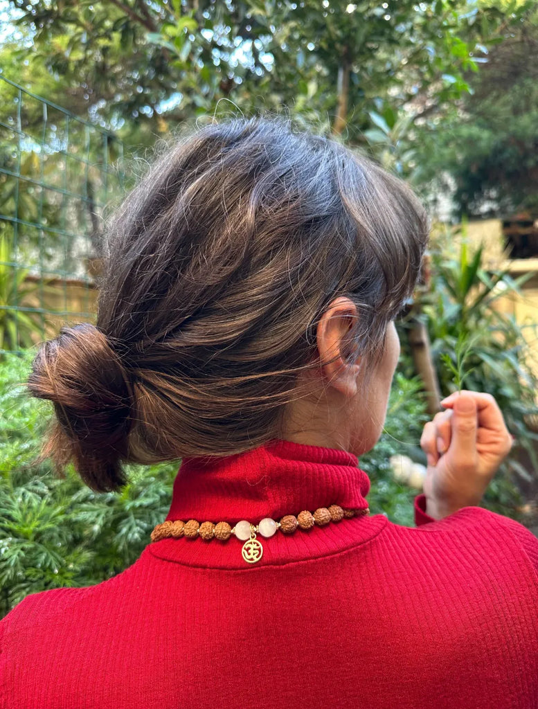 japamala in selenite e rudraksha indossata con pendente Om in argento dorato posato dietro la nuca