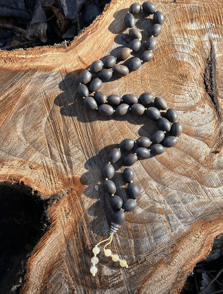 Mālā 54 Semi di Loto con elemento guru in argento, decori in pietra Calcite distesa su tronco per visione d'insieme